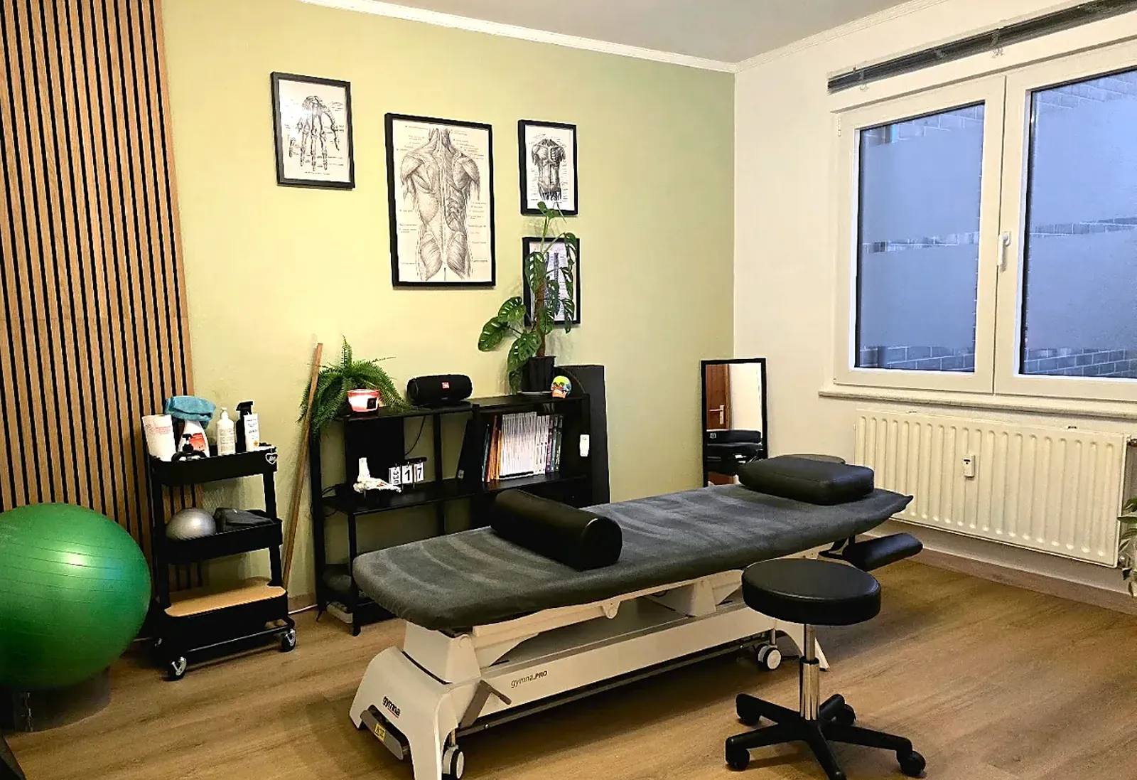 Salle de soins du cabinet M.P. Health & Care : table de traitement électrique, planches d'anatomie, matériel d'exercice